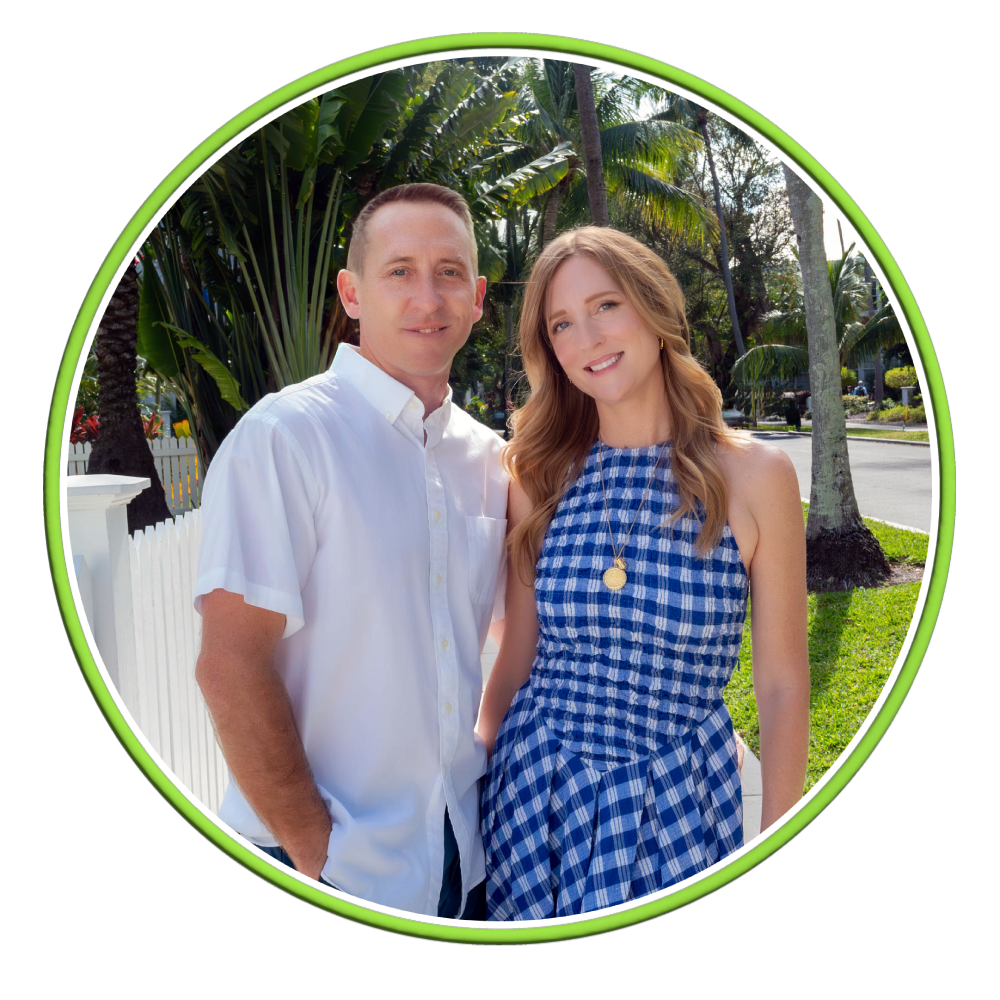 A smiling couple poses together outdoors, surrounded by lush greenery and palm trees, showcasing a vibrant and cheerful atmosphere.